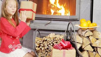 Adorable little girl opening christmas gifts near fireplace video