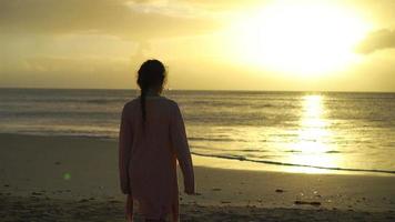 entzückendes glückliches kleines Mädchen, das bei Sonnenuntergang am weißen Strand spazieren geht video