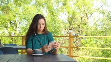 mulher usando app em smartphone no café bebendo café sorrindo e mensagens de texto no celular. bela jovem profissional feminina com telefone móvel. video