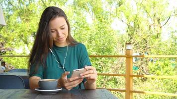 mujer joven llamando con teléfono celular mientras está sentada sola en la cafetería durante el tiempo libre. mujer atractiva con una linda sonrisa conversando con el teléfono móvil mientras descansa en el café video