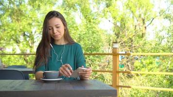 vrouw met smartphone in cafe drinken koffie glimlachen en sms'en Aan mobiel telefoon. portret van mooi jong meisje video