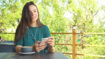 femme utilisant l'application sur smartphone dans un café buvant du café en souriant et envoyant des SMS sur son téléphone portable. belle jeune femme professionnelle avec téléphone portable. video