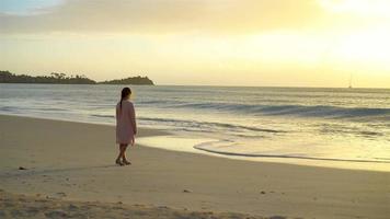 Adorable happy little girl walking on white beach at sunset. video