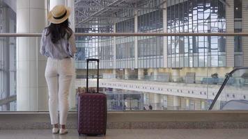 jovem de chapéu com bagagem no aeroporto internacional caminhando com sua bagagem. passageiro da companhia aérea em um saguão do aeroporto à espera de aeronaves de voo video