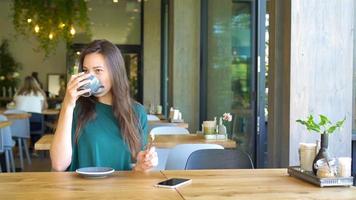 Young woman calling with cell telephone while sitting alone in coffee shop during free time. Attractive female with cute smile having talking conversation with mobile phone while rest in cafe video