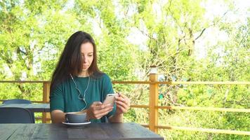 donna con smartphone nel bar potabile caffè sorridente e sms su mobile Telefono. ritratto di bellissimo giovane ragazza video