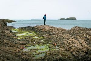 Male person stand on rugged shore enjoy seascape alone outdoors.Game of thrones filming location fishing village in Ballintoy. Northern Ireland photo