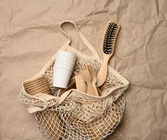 white string bag with disposable paper dishes and wooden forks on brown kraft paper photo