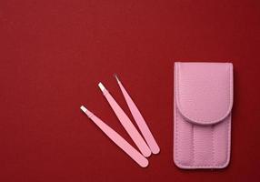 pink leather case with various metal eyebrow tweezers on a red background photo