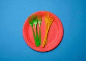 green, orange plastic forks and empty red paper disposable plates on a blue background