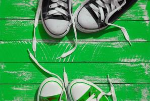 Two pairs of sneakers youth with untied laces on the green surface photo