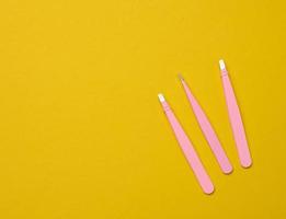 various metal eyebrow tweezers on a yellow background photo