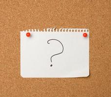 a white sheet of paper with a question mark attached with red buttons to a brown cork board photo