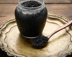 fresh black paddlefish caviar in a wooden brown spoon and a full can of caviar on a wooden table photo