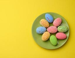 decorative easter eggs in a round green ceramic plate on a yellow background, top view, photo