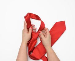 two female hands hold a red silk tie on a white background photo