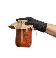 female hand in a black latex glove holds a glass jar with canned tomatoes in sauce photo