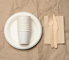 disposable round white paper plates and cups on brown paper background, top view photo