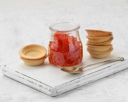 red caviar in a glass jar and round tartlets on a white table photo