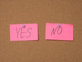 two pink sheets are hanging on a brown cork board, the inscription is yes no photo