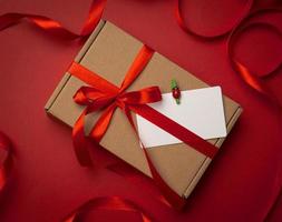 rectangular brown cardboard box tied with a silk red ribbon on a red background photo