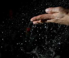 mano femenina y gotas de agua voladoras sobre un fondo negro foto