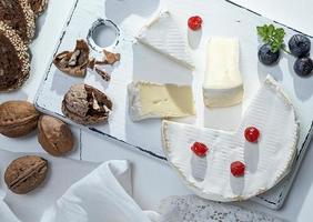 queso camembert redondo rebanado en una tabla de madera blanca foto