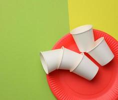 stack of white paper cups and red round plates on a green background. photo