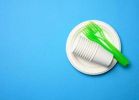 green plastic forks and empty white paper disposable plates on a blue background, photo