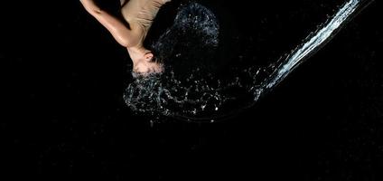hermosa mujer de apariencia caucásica con cabello negro en gotas de agua sobre un fondo negro foto