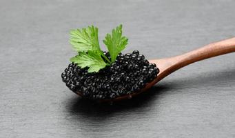 caviar de pez espátula negro granulado fresco en una cuchara de madera marrón sobre un fondo negro, foto