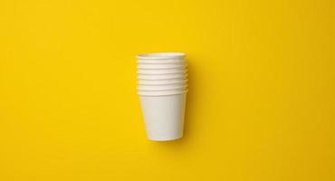 stack of white paper cups on a yellow background. Plastic rejection concept, zero waste photo