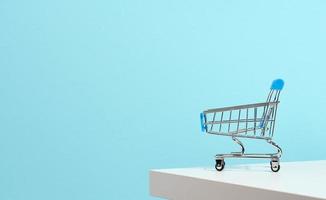 empty miniature shopping cart on blue background. Seasonal sale, copy space photo