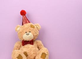 teddy beige bear in a red cap sits on a purple background photo