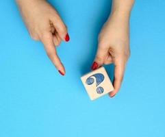 mano femenina sosteniendo un cubo de madera con un signo de interrogación sobre un fondo azul, el concepto de respuestas y preguntas foto