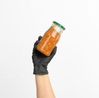 female hand in a black glove holds a glass jar with cooked beans in tomato sauce photo