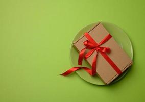 caja rectangular de cartón marrón atada con una cinta roja y sobre una cerámica verde foto