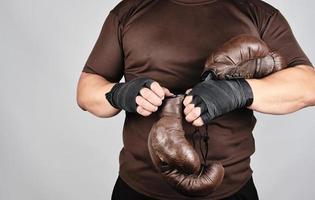 young man stands and puts on his hands very old vintage brown boxing gloves photo