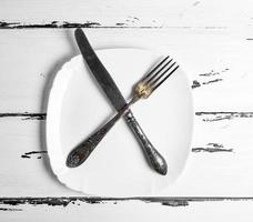 iron vintage fork with knife lying on a blank white square plate photo