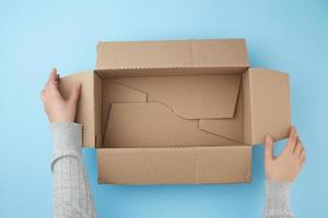 female hands are holding an empty open box of brown cardboard, top view photo