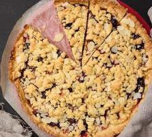 baked round crumble pie with plum cut into pieces on a black background photo