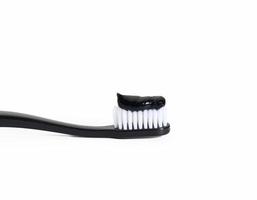 black  plastic toothbrush with black charcoal paste on white background photo