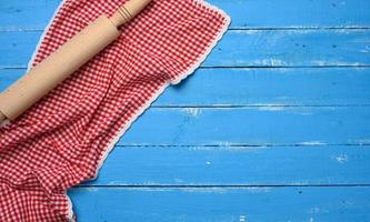 pasador rodante y servilleta de cocina de algodón rojo y blanco doblada sobre un fondo azul de madera, foto