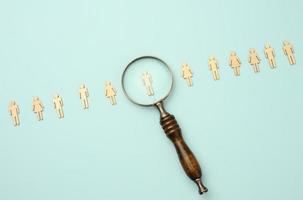 wooden men and a magnifying glass on a blue background. Recruitment concept, search for talented and capable employees photo