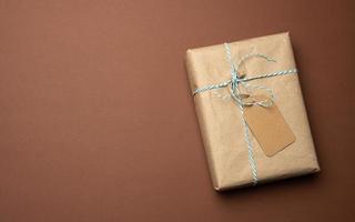 box wrapped in brown kraft paper and tied with rope, gift on a brown background photo