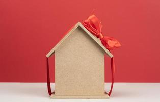 model of a wooden house tied with a red silk ribbon on a red background, concept of real estate purchase photo