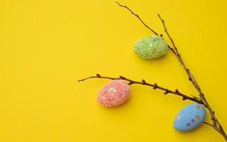 huevos de pascua decorativos cuelgan de una rama, fondo amarillo foto