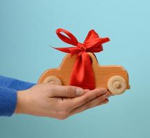 female hand holding wooden toy car with red ribbon on blue background photo