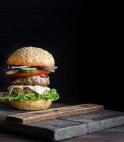 large burger with two fried cutlets, cheese and vegetables photo