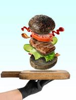 A hand holds a wooden cutting board and flying hamburger ingredients photo